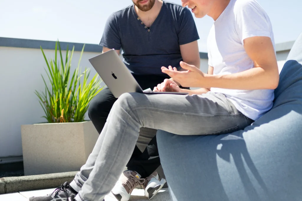Colleagues collaborating on a project with a laptop on a sunny rooftop lounge.