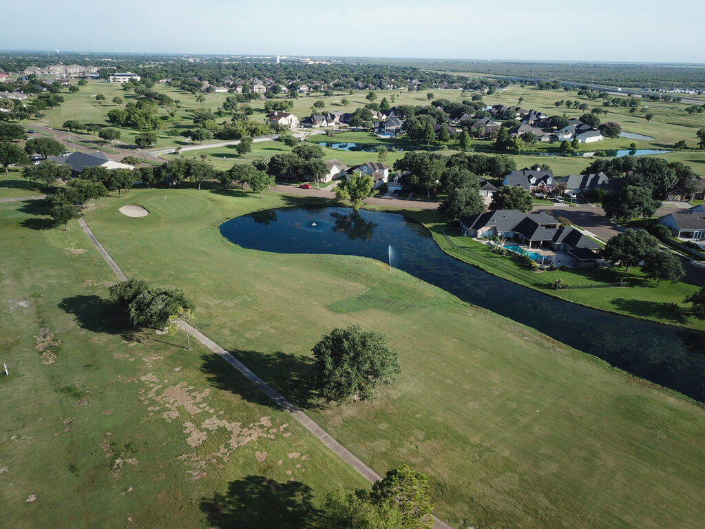 Aerial view of a golf course with a pond and surrounding residential homes.