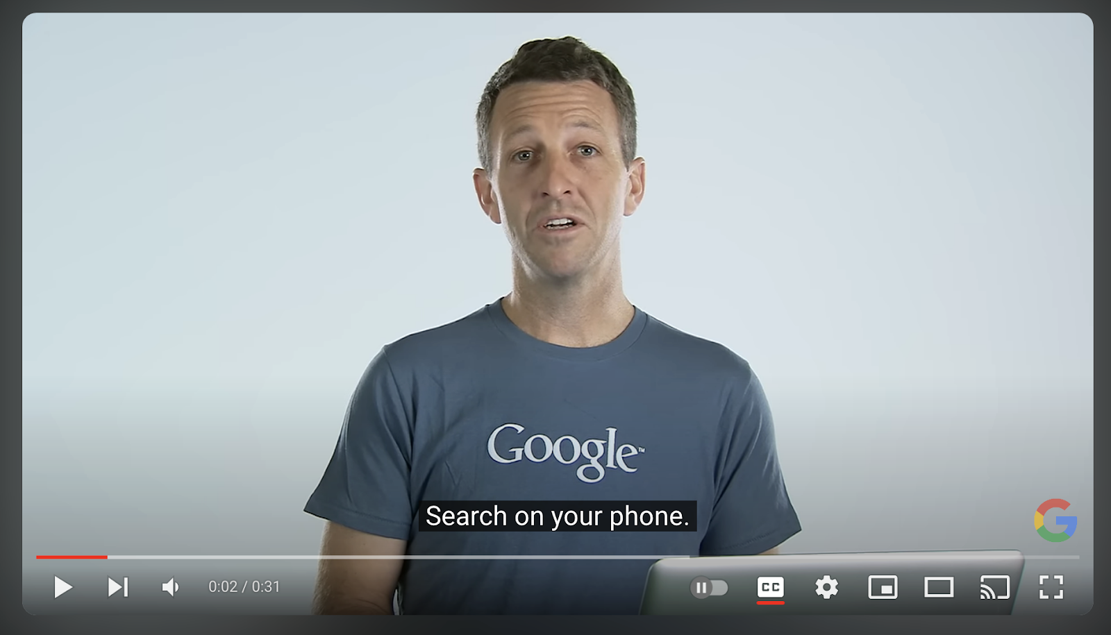 A man wearing a Google t-shirt speaking in a video with the subtitle 'Search on your phone' displayed at the bottom of the screen.