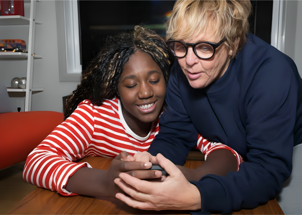 Two people smiling while looking at a device together.